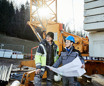 Zwei Männer vor einem Kran mit Bauplänen